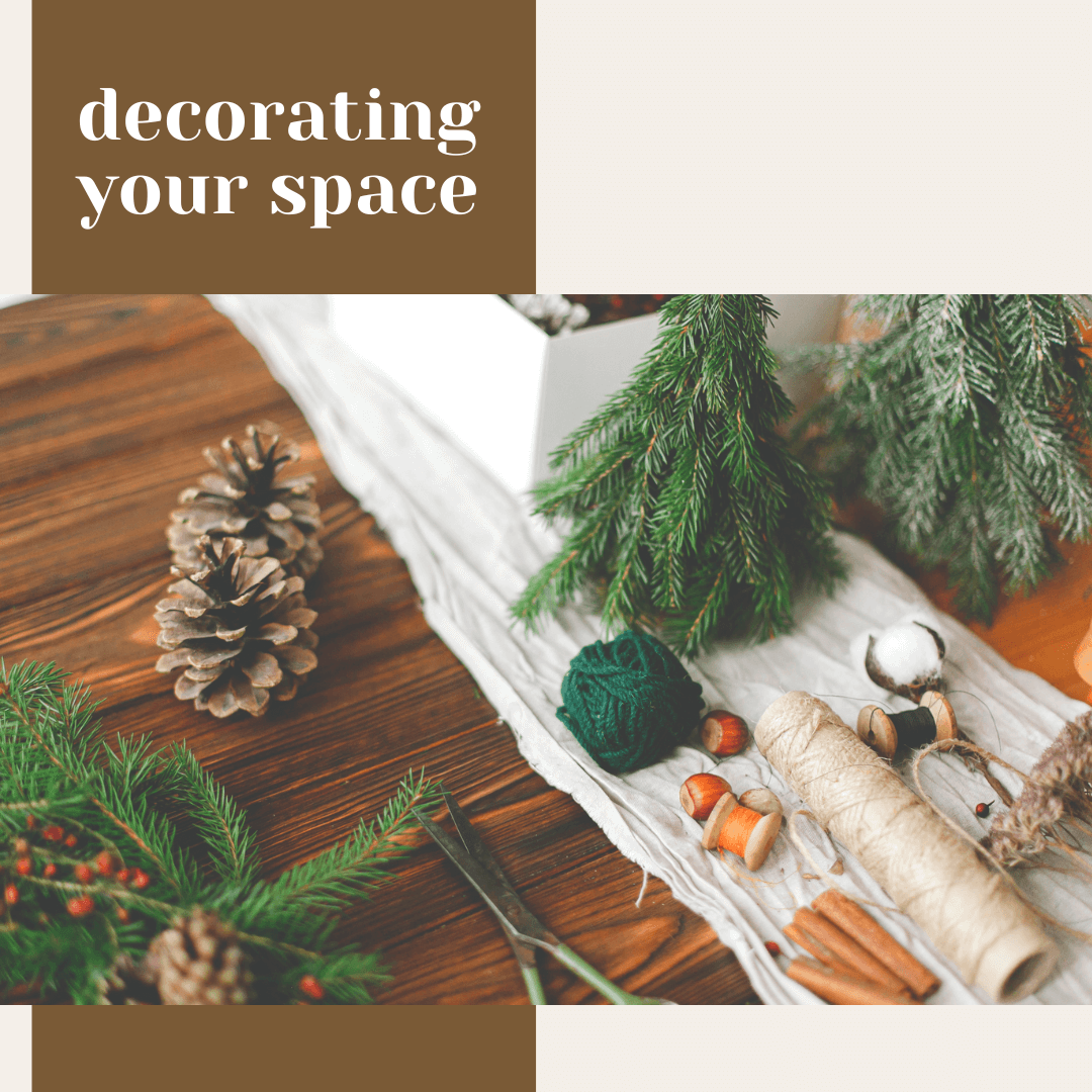  Holiday place setting with a rolled napkin tied in twine, star anise, hazelnut, and dried orange slice on a white plate, with glowing candles in the background and the words ‘adorning the table.